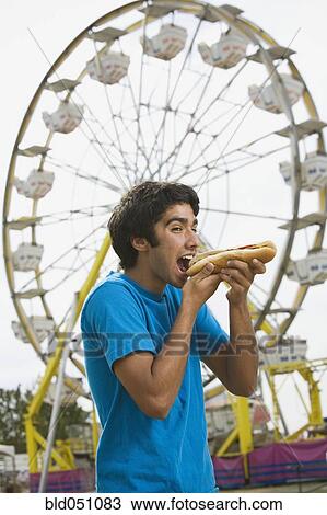 Stock Image - Mixed Race teenaged boy eating hot dog at carnival. Fotosearch