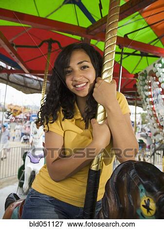 Stock Photo - Mixed Race teenaged girl on carousel horse. Fotosearch