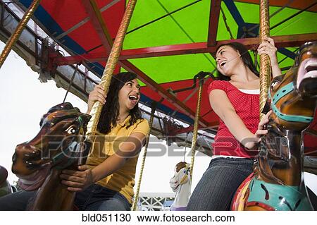 Stock Image - Mixed Race teenaged girls on carousel horse. Fotosearch