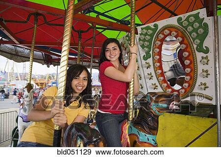 Stock Photo - Mixed Race teenaged girls on carousel horse. Fotosearch