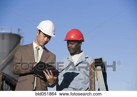 Multi-ethnic businessman and construction worker looking at paperwork View Large Photo Image Picture - Multi-ethnic businessman and construction worker looking at paperwork. Fotosearch