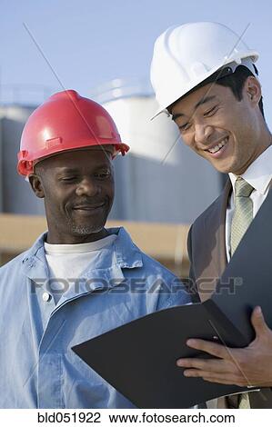 Multi-ethnic businessman and construction worker looking at paperwork View Large Photo Image Stock Image - Multi-ethnic businessman and construction worker looking at paperwork. Fotosearch