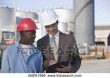 Multi-ethnic businessman and construction worker looking at paperwork View Large Photo Image Stock Photograph - Multi-ethnic businessman and construction worker looking at paperwork. Fotosearch