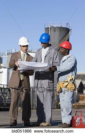 Multi-ethnic businessman and construction workers looking at blueprints View Large Photo Image Stock Photograph - Multi-ethnic businessman and construction workers looking at blueprints. Fotosearch