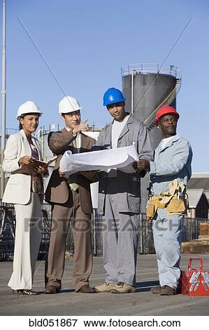 Multi-ethnic businesspeople and construction workers looking at blueprints View Large Photo Image Stock Photo - Multi-ethnic businesspeople and construction workers looking at blueprints. Fotosearch