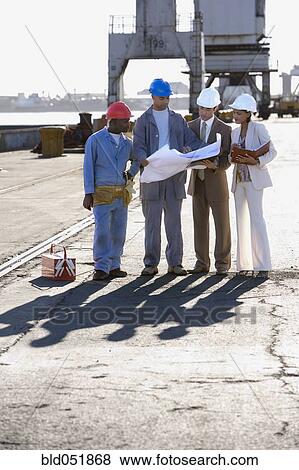 Multi-ethnic businesspeople and construction workers looking at blueprints View Large Photo Image Stock Photo - Multi-ethnic businesspeople and construction workers looking at blueprints. Fotosearch