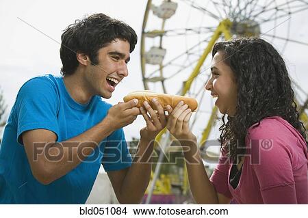 Picture - Multi-ethnic couple eating hot dog at carnival. Fotosearch