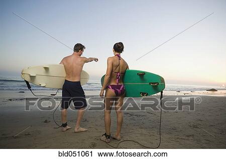 Stock Image - Multi-ethnic couple holding surfboards. Fotosearch