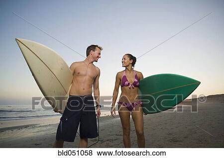 Stock Photo - Multi-ethnic couple holding surfboards. Fotosearch