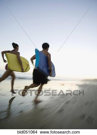 Multi-ethnic couple running with surfboards View Large Photo Image Picture - Multi-ethnic couple running with surfboards. Fotosearch