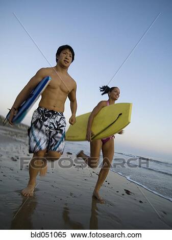 Stock Photography - Multi-ethnic couple running with surfboards. Fotosearch