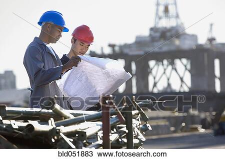 Stock Image - Multi-ethnic male construction workers looking at blueprints. Fotosearch