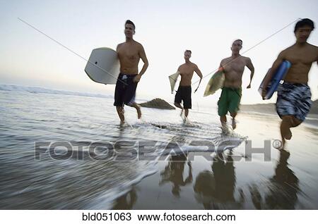 Stock Image - Multi-ethnic men running with surfboards. Fotosearch