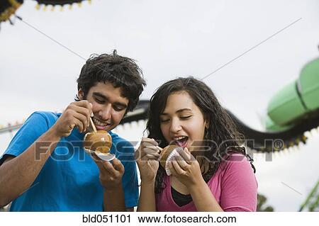 Stock Image - Multi-ethnic teenaged couple eating candied apples. Fotosearch