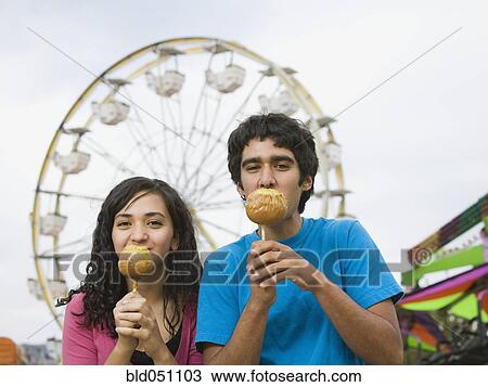 Stock Image - Multi-ethnic teenaged couple eating candied apples. Fotosearch