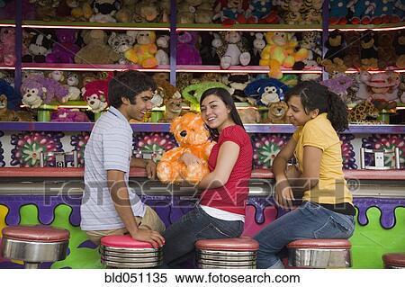Stock Photography - Multi-ethnic teenaged friends at carnival booth. Fotosearch