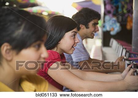 Stock Image - Multi-ethnic teenaged friends playing carnival game. Fotosearch