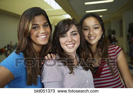 Stock Image - Multi-ethnic teenaged girls hugging in school hallway. Fotosearch