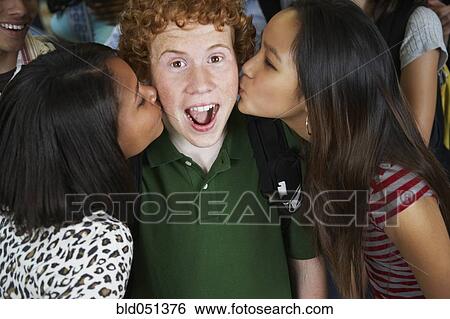Stock Photograph - Multi-ethnic teenaged girls kissing boy on cheeks. Fotosearch