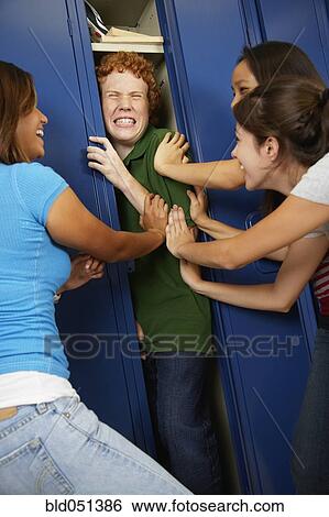 Stock Photograph - Multi-ethnic teenaged girls pushing boy into school locker. Fotosearch