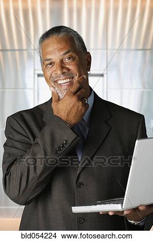 Picture - African businessman holding laptop. Fotosearch