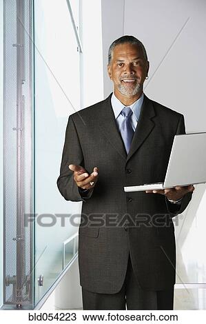 Stock Image - African businessman holding laptop. Fotosearch
