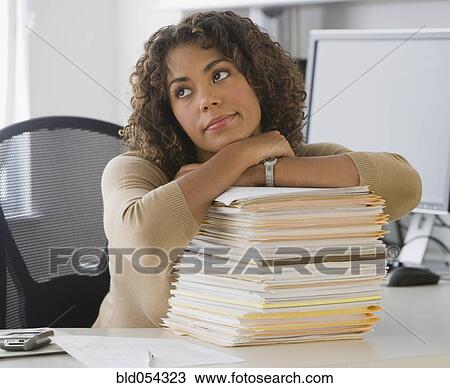 Stock Image - African businesswoman leaning on stack of paperwork. Fotosearch