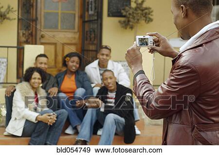 Stock Photo - African man taking photograph of friends. Fotosearch