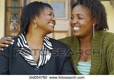 Stock Image - African mother and adult daughter smiling at each other. Fotosearch