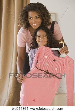 Picture - African mother holding dress up in front of daughter. Fotosearch
