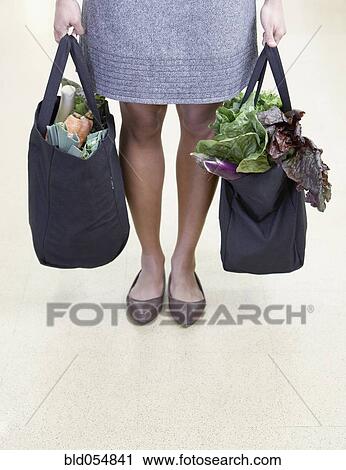 Stock Image - African woman holding reusable grocery bags. Fotosearch
