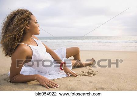 Stock Image - African woman laying on sand. Fotosearch