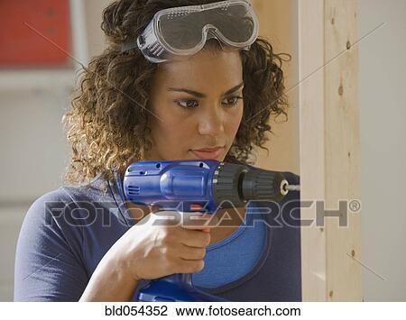 Stock Image - African woman using cordless drill. Fotosearch