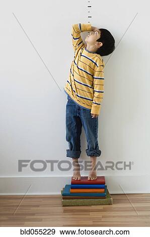 Stock Photo - Asian boy standing on books in front of height markers. Fotosearch