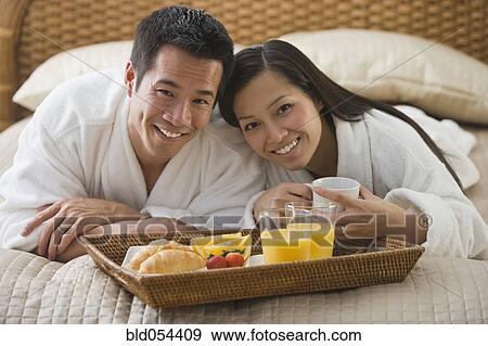 Stock Photo - Asian couple eating breakfast in bed. Fotosearch
