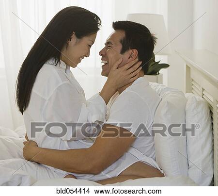 Picture - Asian couple hugging in bed. Fotosearch