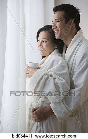 Stock Image - Asian couple in bathrobes hugging. Fotosearch