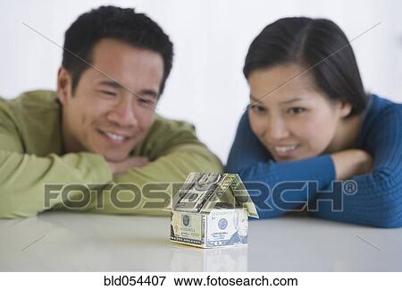 Picture - Asian couple looking at house made of money. Fotosearch - Search Stock Photography, Photos, Prints, Images, and Photo Clipart