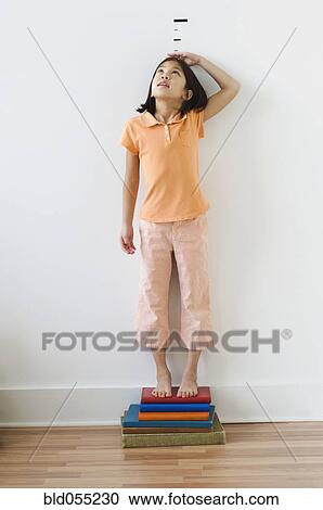 Stock Image - Asian girl standing on books in front of height markers. Fotosearch