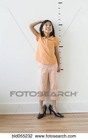 Stock Image - Asian girl wearing mother’s shoes in front of height markers. Fotosearch