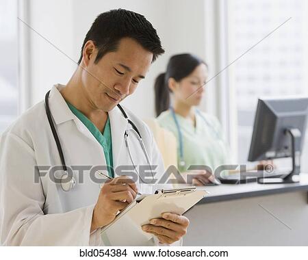 Picture - Asian male doctor writing on chart. Fotosearch