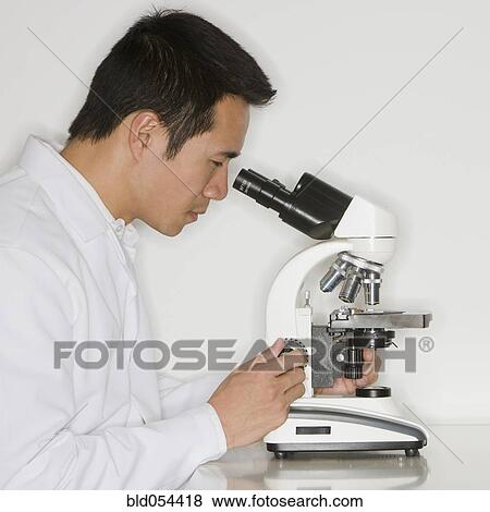 Stock Photo - Asian male scientist looking into microscope. Fotosearch