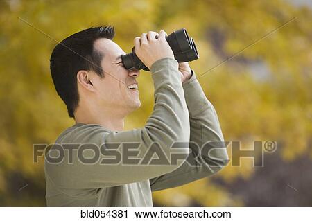 Stock Image - Asian man looking through binoculars. Fotosearch