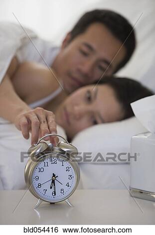 Stock Photograph - Asian man touching alarm clock. Fotosearch