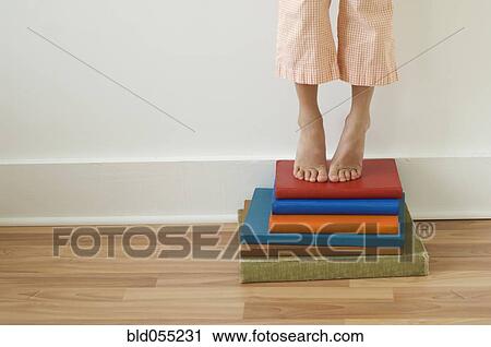 Stock Image - Girl standing on tiptoes on stack of books. Fotosearch