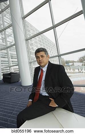 Hispanic businessman sitting on edge of table View Large Photo Image Stock Photograph - Hispanic businessman sitting on edge of table. Fotosearch
