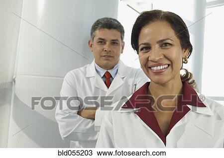Hispanic female doctor with male doctor in background View Large Photo Image Stock Image - Hispanic female doctor with male doctor in background. Fotosearch