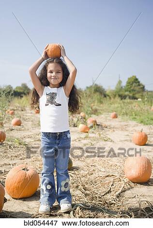 Hispanic girl holding pumpkin on head View Large Photo Image Stock Photo - Hispanic girl holding pumpkin on head. Fotosearch
