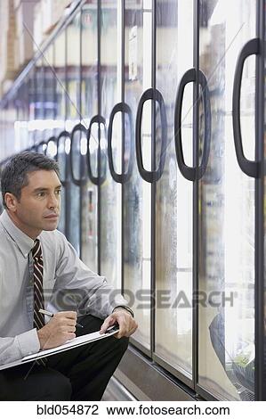 Stock Image - Hispanic grocery store manager writing on clipboard. Fotosearch