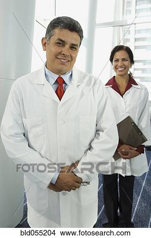 Hispanic male doctor with female doctor in background View Large Photo Image Picture - Hispanic male doctor with female doctor in background. Fotosearch